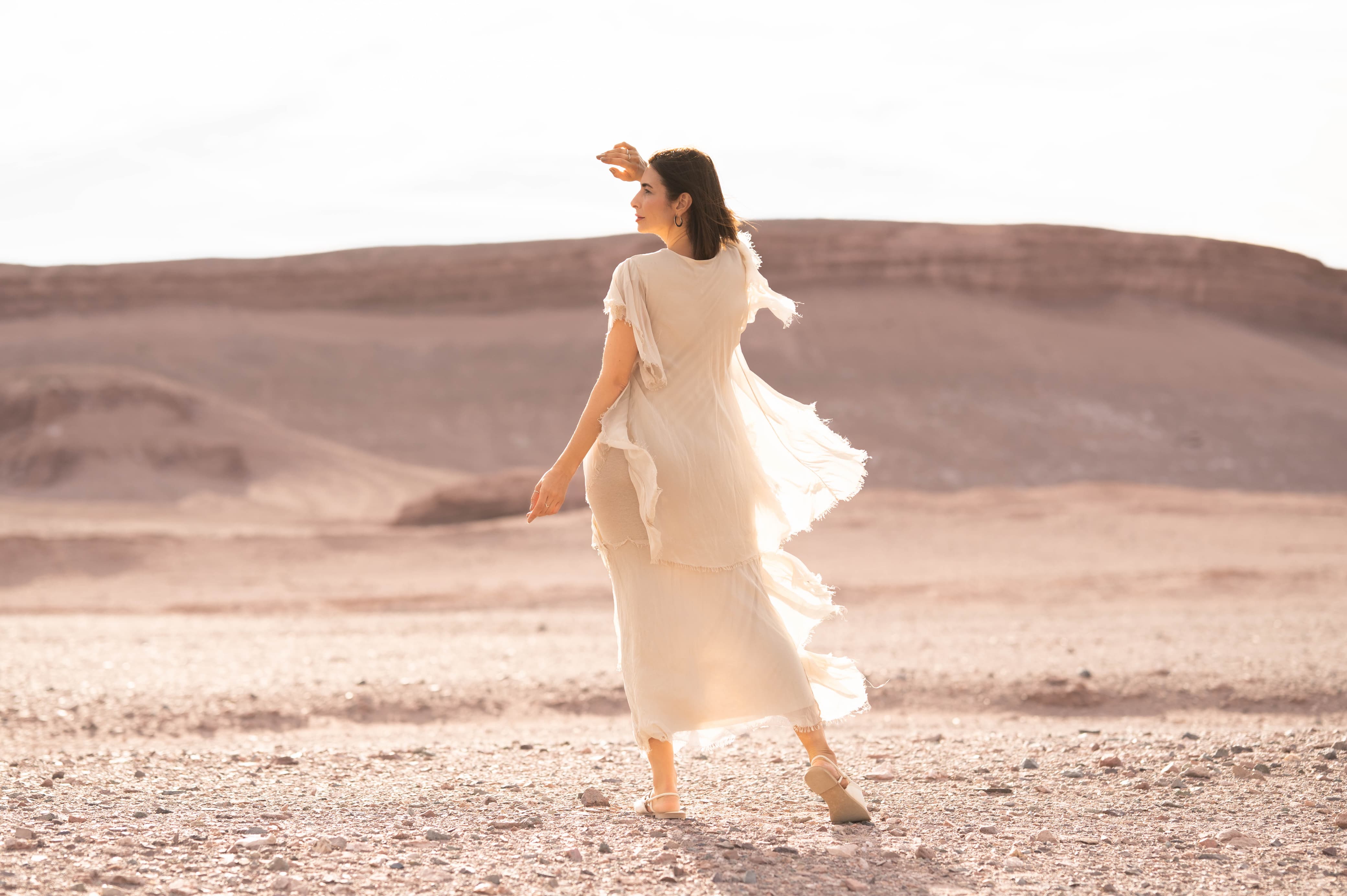 Mulher caminhando no deserto vestindo o Vestido Ilha de Elba em tom claro, com tecido leve e fluido.